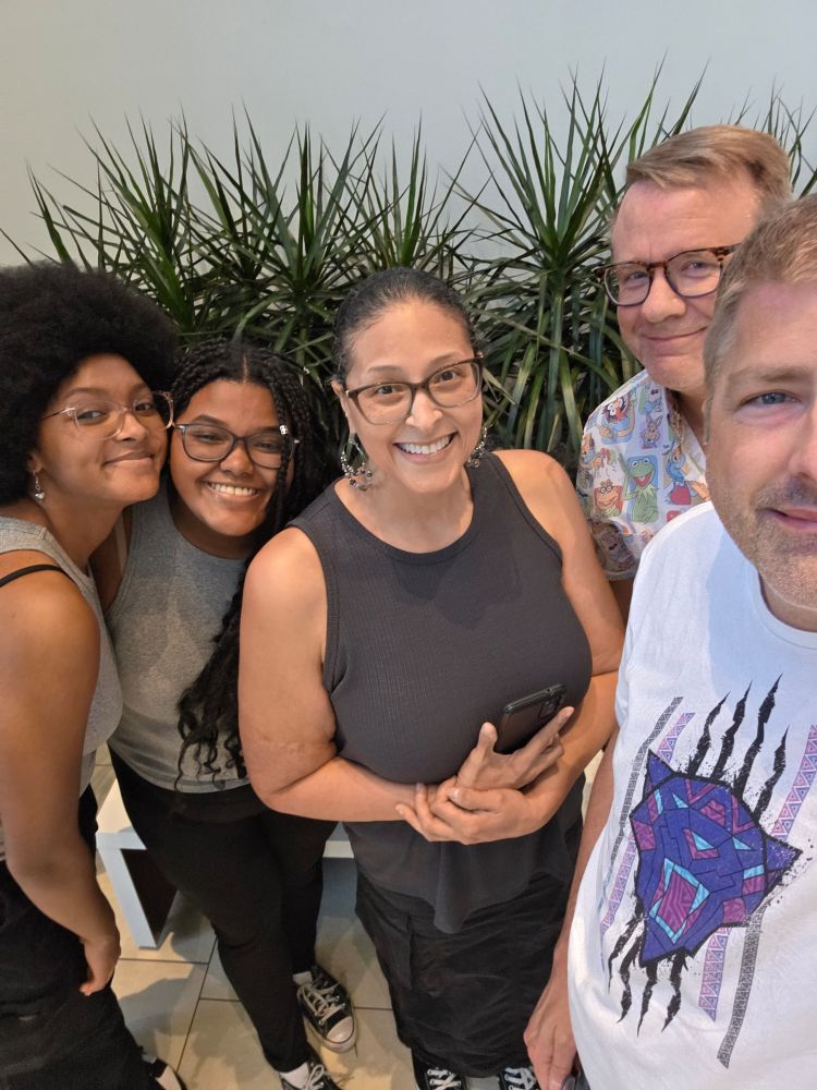 A photo of tom (to the very right, wearing a Black Panther themed shirt, with Quinn, Danielle, Ellie, and Cianna, three wonderful women. They are all wearing gray and Black clothing and Quinn is wearing a shirt featuring the Muppets