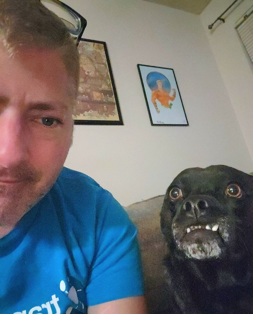 Tom on camera left, Mike the dog on the right. Mike has a big grin for the camera, he is a pit/lab/pug black dog , small, ahout 30lbs. He has premature gray in his muzzle, just like Tom. 