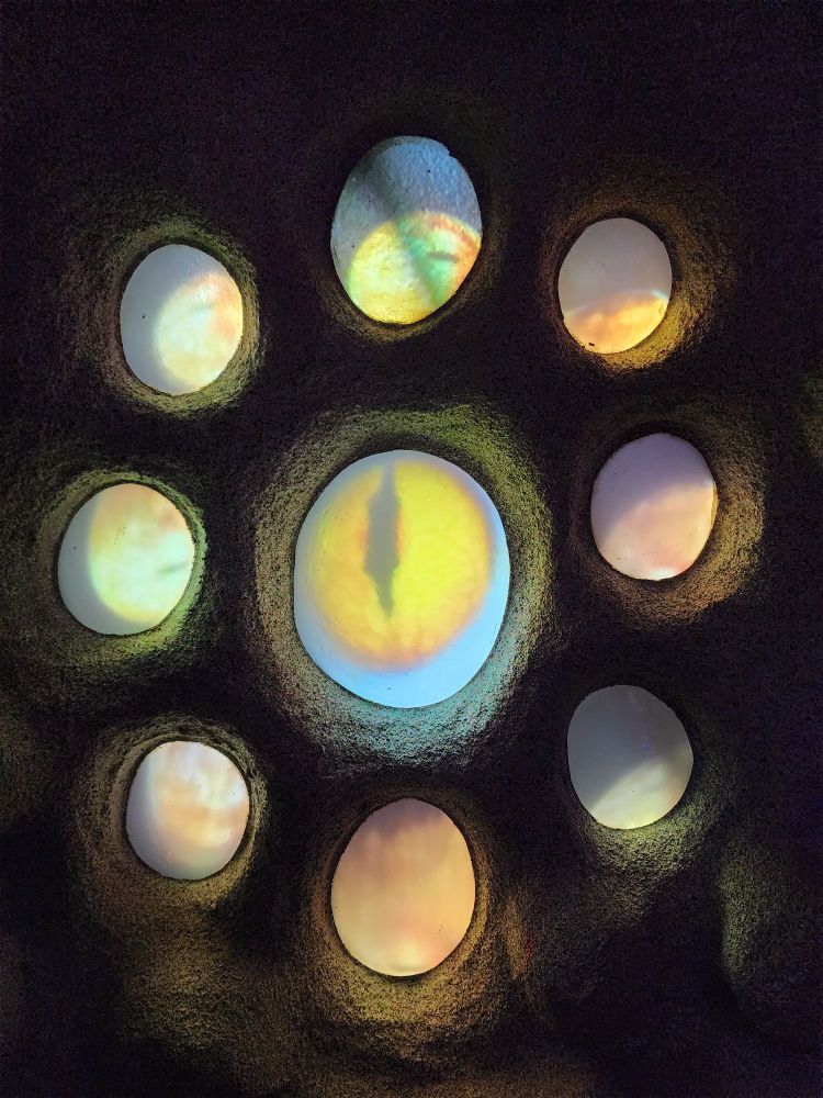 A mosaic that is three dimensional, showing a large eye that resembles a cat's eye, surrounded by 8 smaller circles that somewhat resemble eyes, but we're more or a greenish yellow white luminescence. 