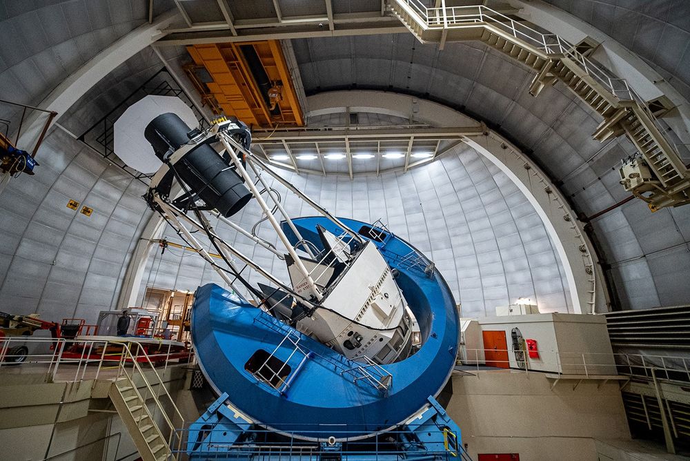 DESI’s instrument, a long black cylinder supported by the metal framework of the telescope, points at the domed ceiling.