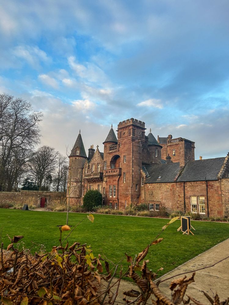 Wide-angle shot of a 13th century country house with many turrets, ramparts and a small patch of grass. 