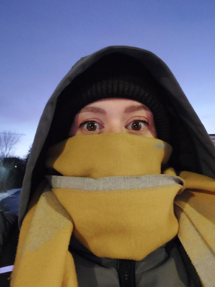 A woman wearing a winter jacket, a tuque, and a yellow scarf covering the bottom half of her face.