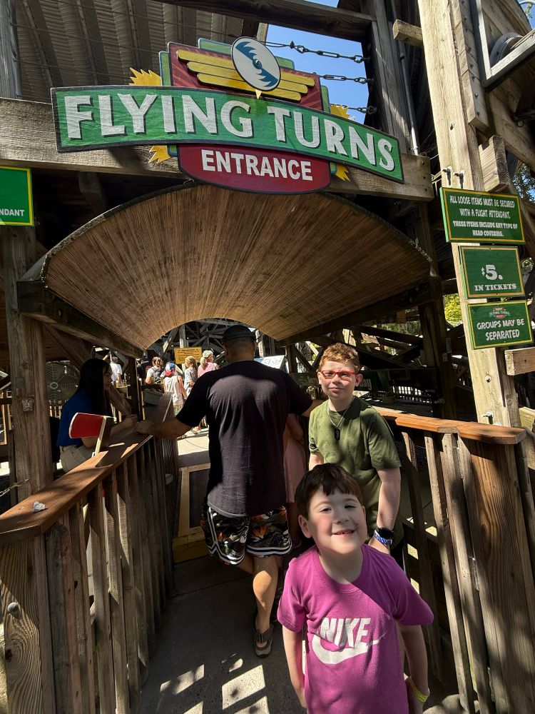 Oldest and youngest sons in front of the entrance to Flying Turns, a wooden bobsled roller coaster at Knoebels Amusement Resort, Elysburg, PA.