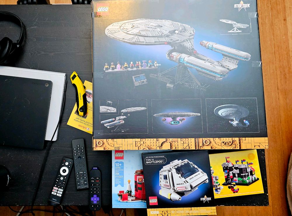 The Star Trek LEGO box, the Type 15 Shuttlepod LEGO box, the Hot Chocolate Stand LEGO box and the Mini Knight's Castle LEGO box on a coffee table with two laptops and 3 remotes