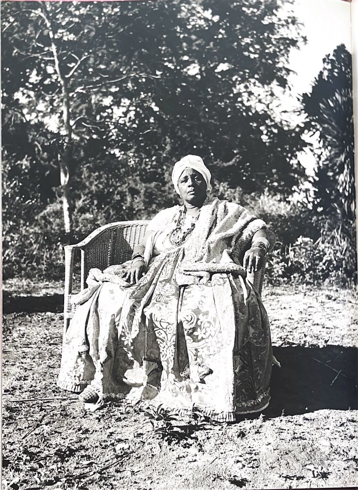 Mãe Stella de Oxossi sentada em uma cadeira de vime num jardim ao ar livre. 