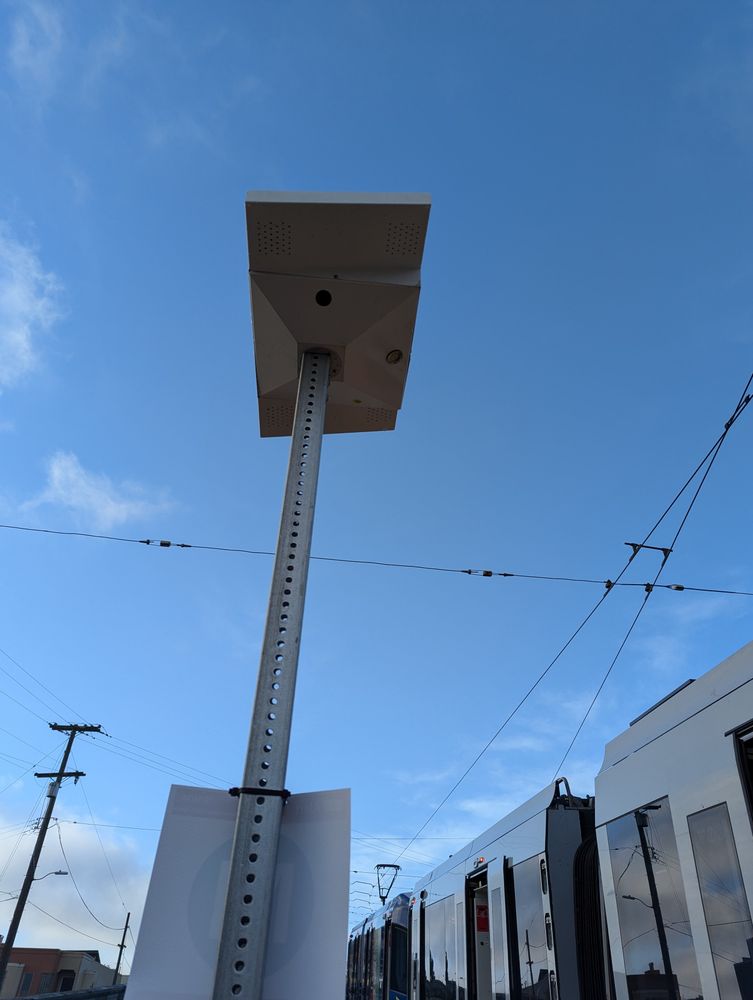 A light fixture on a pole with a light rail vehicle with open doors to the side.
