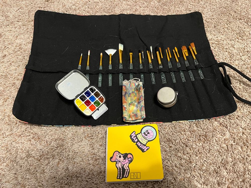 A roll of brushes a watercolor set and small square sketchbook.
