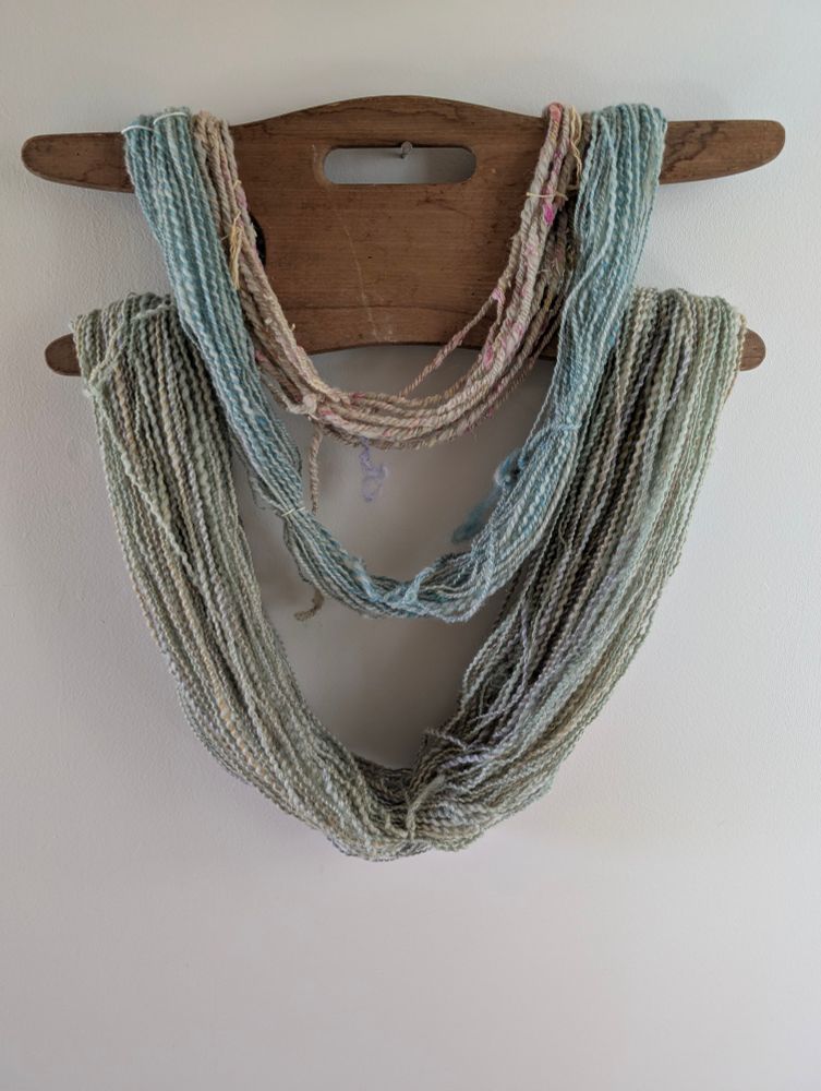 Hand spun yarn in pastel spring colors hanging on a wooden hanger on a white background 