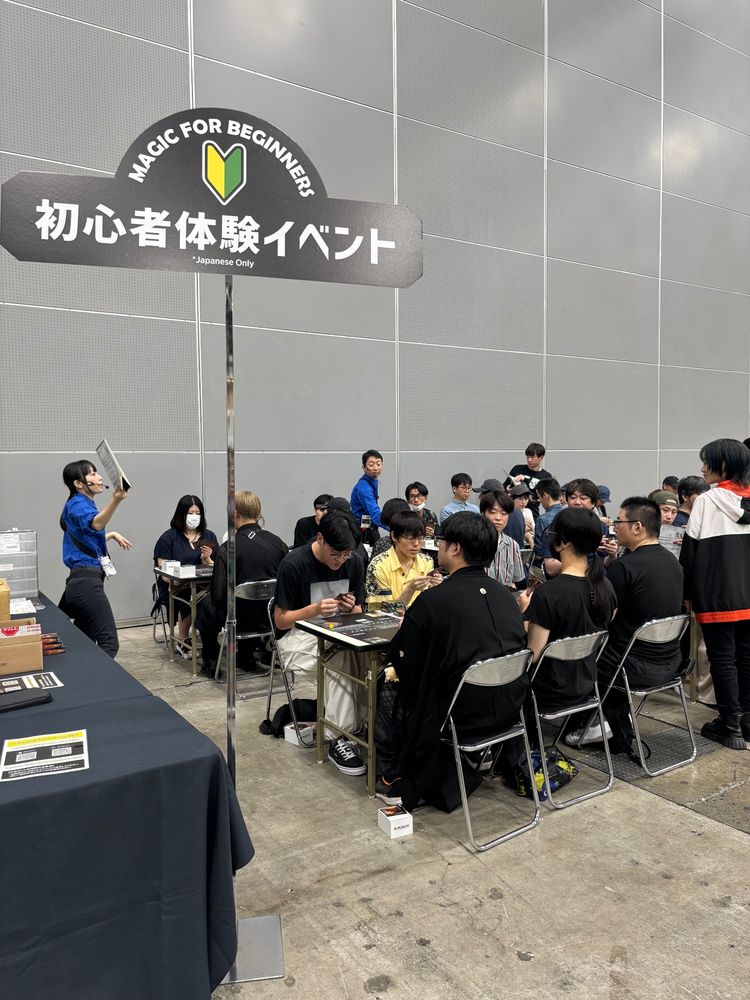 a sign in the event hall says “Magic for Beginners” and there are seated people learning to play