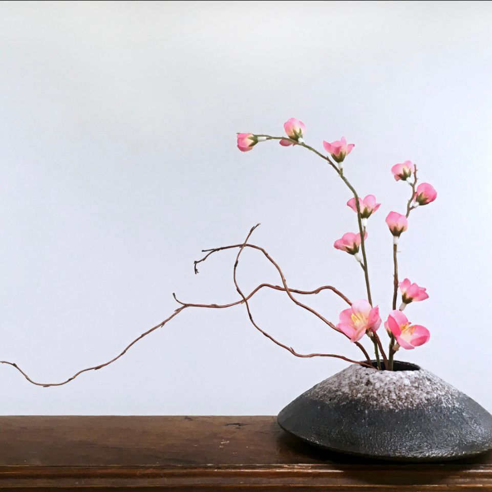 An old photo of a Fuji ikebana vase, containing wispy curly willow branches and a couple sprigs of fake cherry blossom branches. 