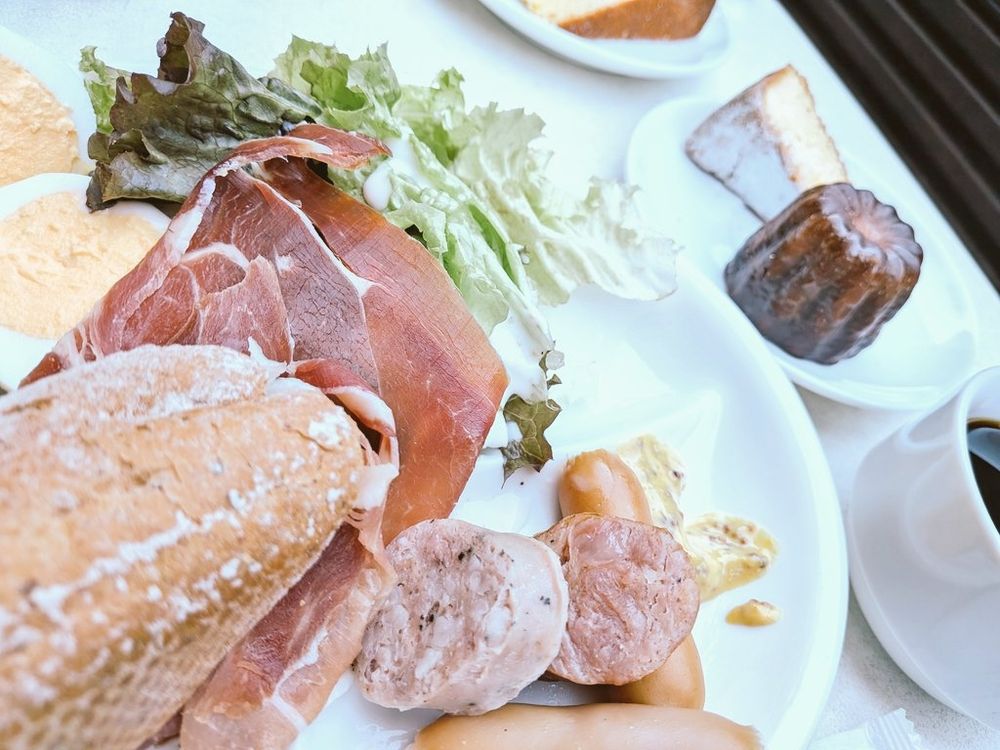 バルのモーニングプレートの写真。加工肉類、サラダ、パン、ゆで卵、カヌレ、ケーキ、コーヒー