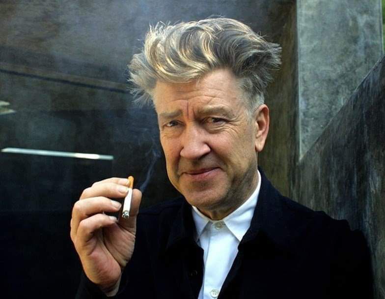 The one and only David Lynch holding a cigarette with a wicked grin on his face. 