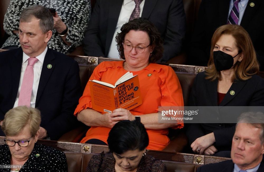 Katie Porter, wearing an orange top, reading a copy of’The Subtle Art of Not Giving a Fuck’