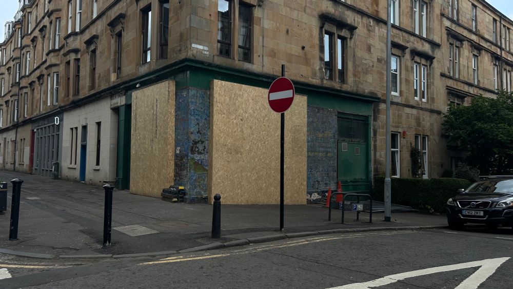 An image of an old shop front situated on the corner of a tenement building. The windows of the shop are covered in brand new chipboard hoardings. The most recent signage from a Turkish shop is obscured but the walls have been scraped to reveal the old signage of a food take away shop - I’m not sure what we called this, Delicatessen was too posh for Glasgow. This was a ‘roll shop’