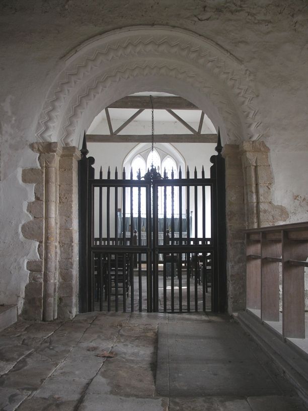 Chancel arch at St. Margaret's, Knotting. The chancel arch is of two orders of bulbous chevron to the west and one plain one to the east. There are clear diagonal tool marks on most surfaces. The arches rest on imposts, the southern of which has been cut away, these in turn rest upon engaged columns with cushion capitals. A label runs around the arch.