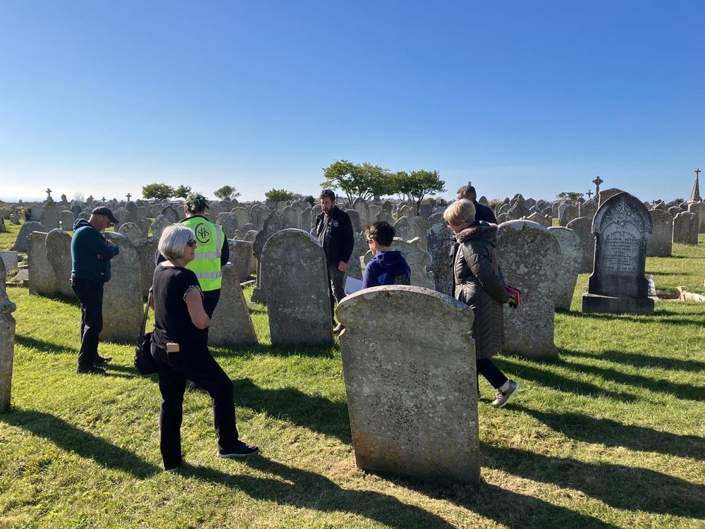 Friends and conservators walking between the tall leaning gravestones in the churchyard on a bright, sunny day.