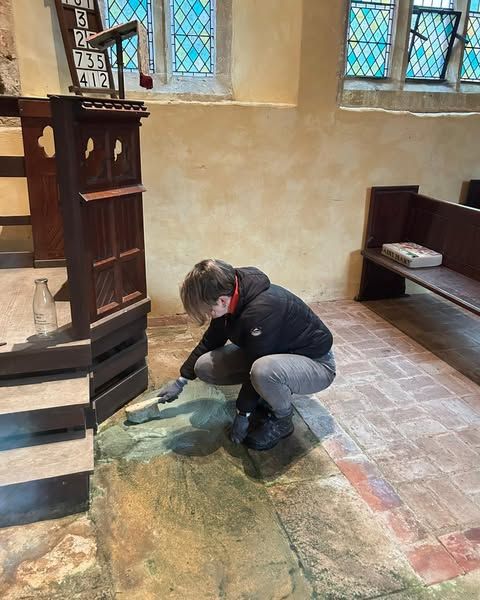 Our Conservation Projects Manager removing green microbiological growth from the floor of a church with a big brush.