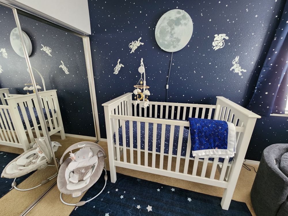 Shot of the nursery with crib and bouncer with the bunny design on the wall in the background