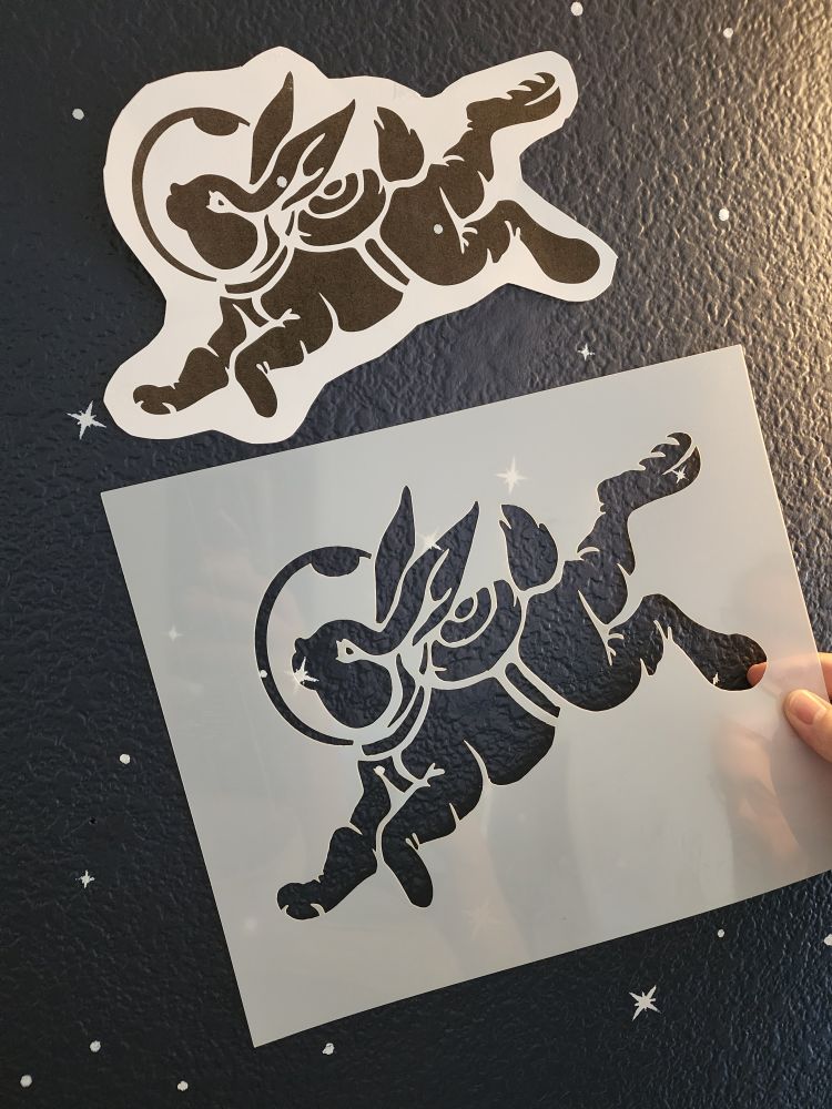Holding up stencil of one of the astronaut bunny designs next to a printout.. the initial set of stencils we got were oddly skewed and we had to get new ones made