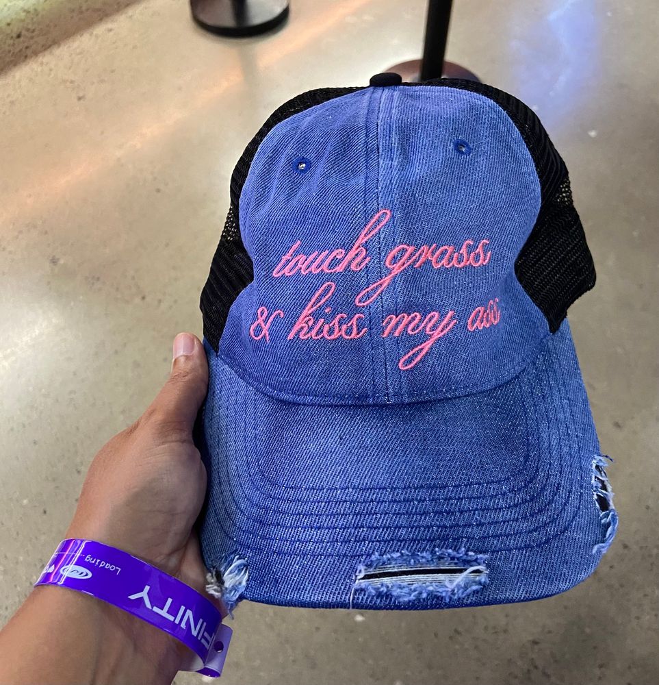 Denim cap with « touch grass and kiss my ass » written on it in pink