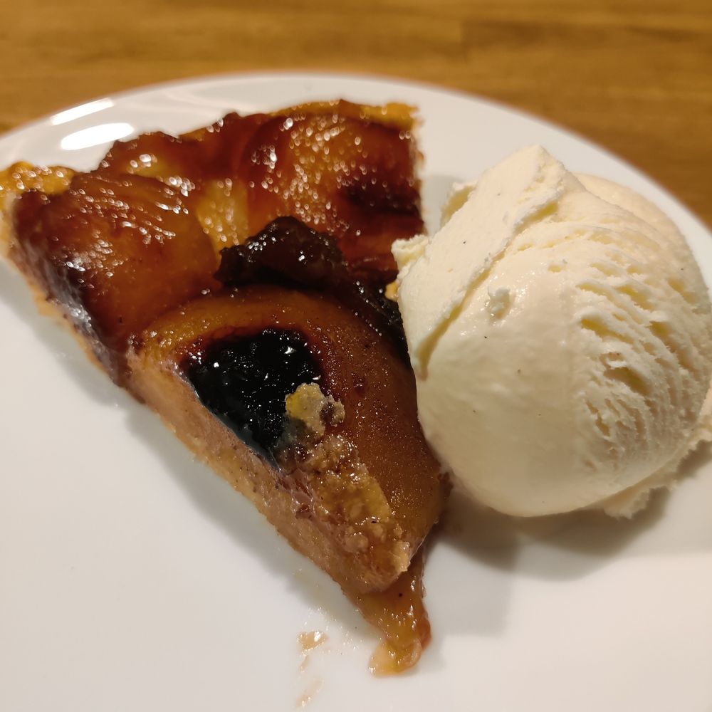 A slice of tarte tatin, darkly caramelised apple on a pastry base. There's a ball of vanilla ice cream next to it.