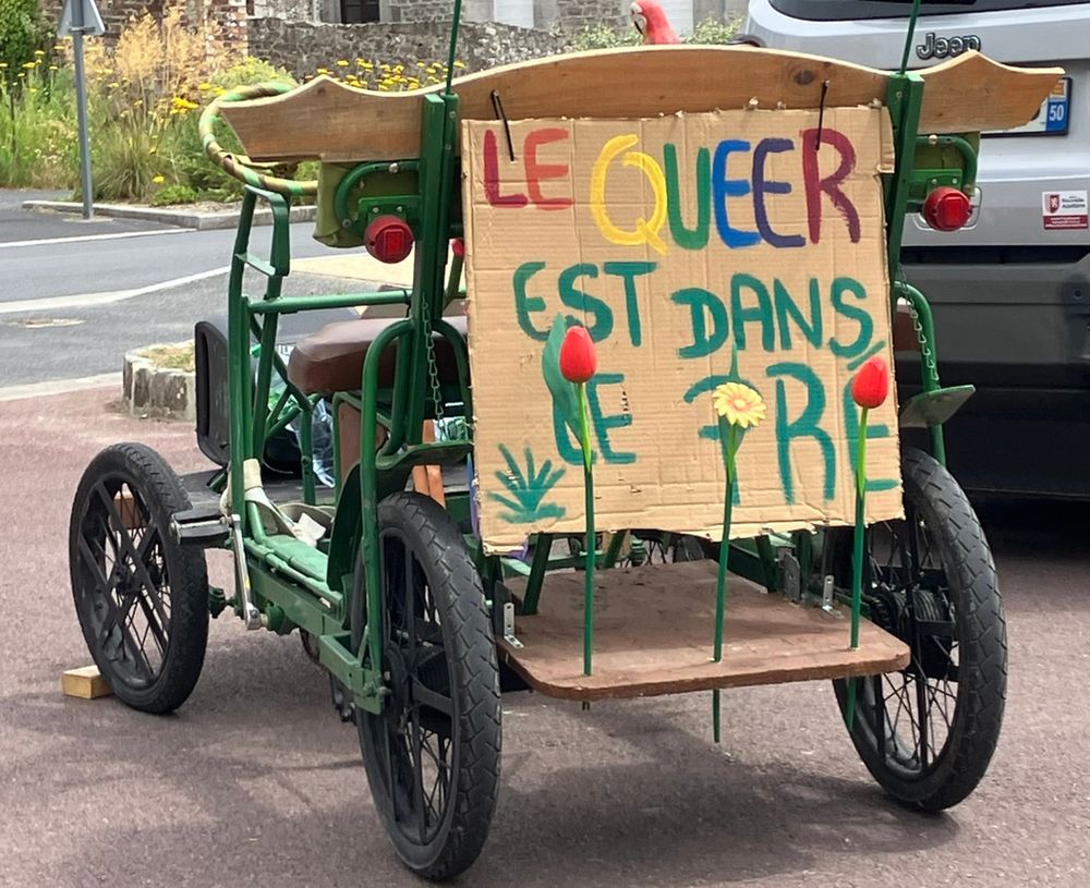 Une Rosalie verte avec à l'arrière un panneau sur lequel est écrit "Le Queer est dans le pré"