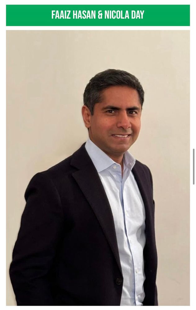Faaiz is a middle aged man in a black two piece suit without a tie, his white top with the top button undone frames his clean shaven brown skin, he has a tidy haircut with black hair, he’s stood in front of an off white wall.