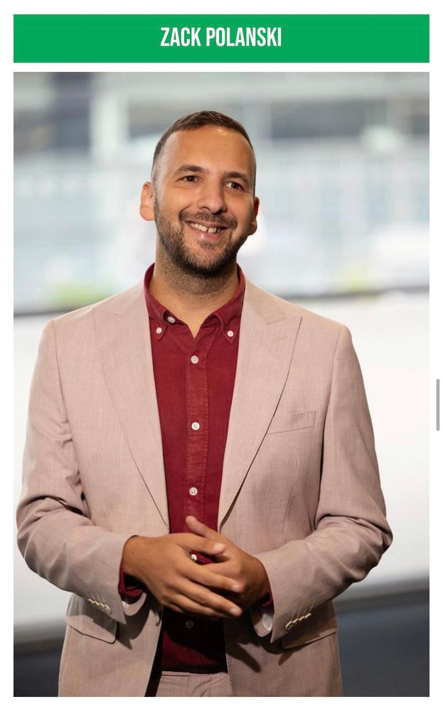 Professional Headshot of Zack Polanski, currently Deputy Leader of GPEW, he is a middle aged man with short hair, white skin, wearing a Beige two piece suit and a red button down collar shirt with no tie.