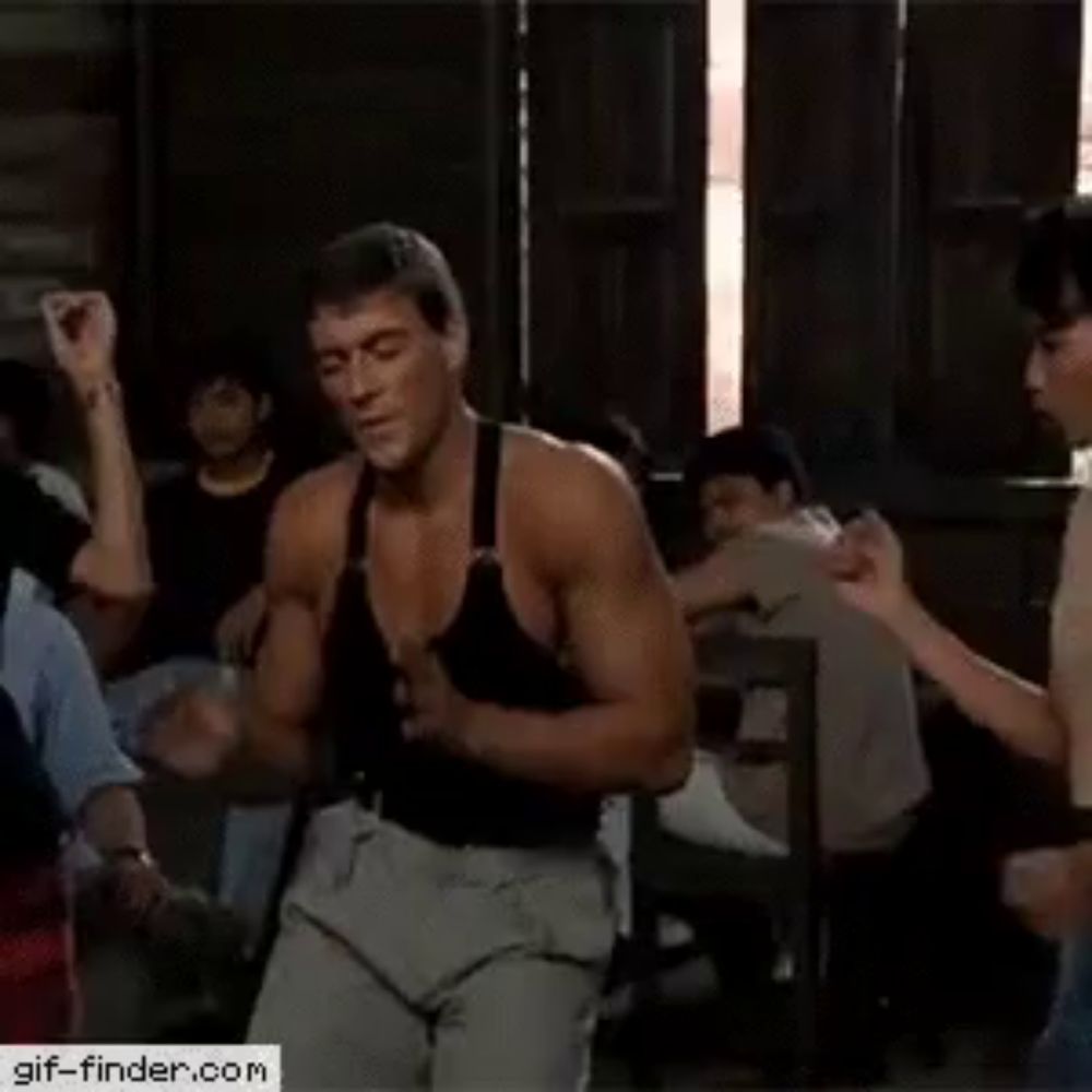 a man in a black tank top is dancing in a room while a woman watches .