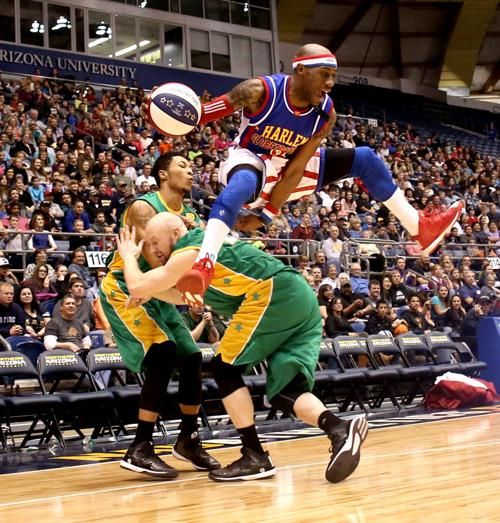 A Harlem Globetrotter basketball player leapfrogging over a Washington Generals player while pushing him into another Washington Generals player.
