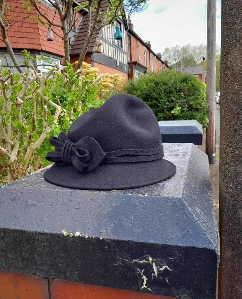 A black wool felt hat with a bow left on a black gate post on a street in Prestwich, Manchester