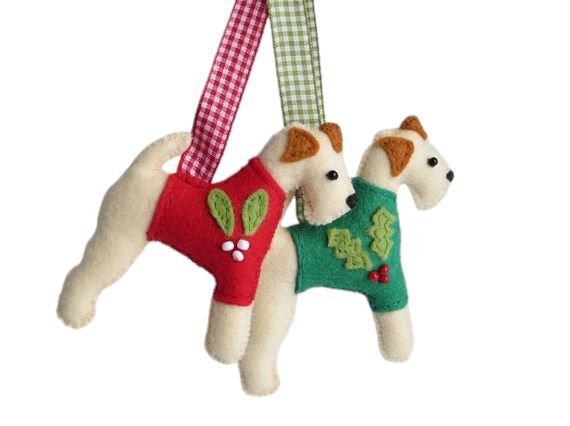 A pair of handmade felt wire fox terrier festive ornaments by misheleneous wearing a red mistletoe and green holly motif christmas jumper. They have coordinating red and green gingham hanging ribbons
