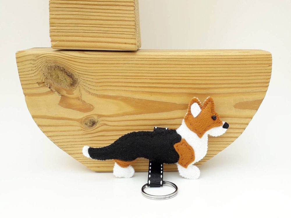 A handmade felt cardigan welsh corgi dog keyring by misheleneous. Displayed against a small boat shaped wooden block