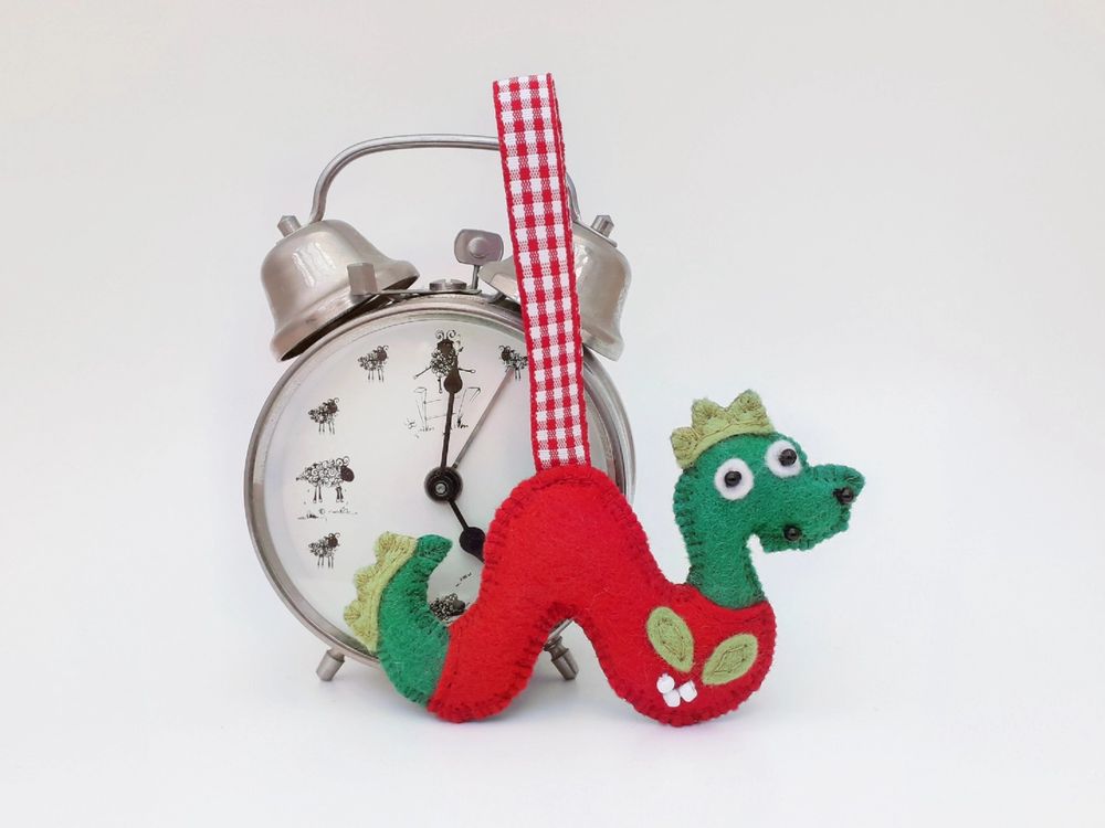 Handmade felt Loch ness monster ornament by misheleneous displayed next to a small retro alarm clock