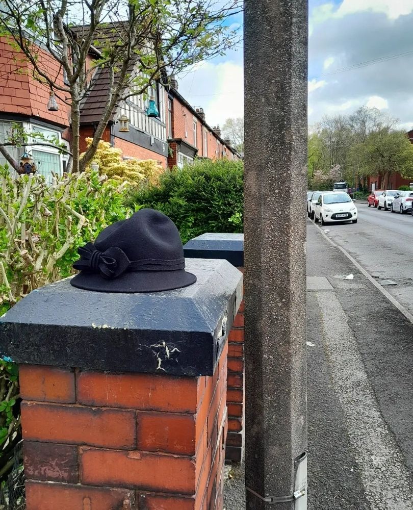 A black wool felt hat with a bow left on a black gate post on a street in Prestwich, Manchester