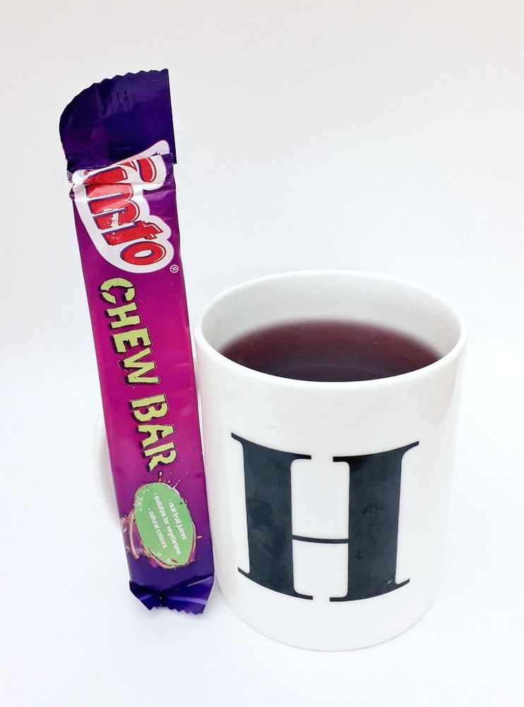 A white mug with a big letter H on it in black type. Its filled with hot vimto and next to a chewy vimto sweety bar