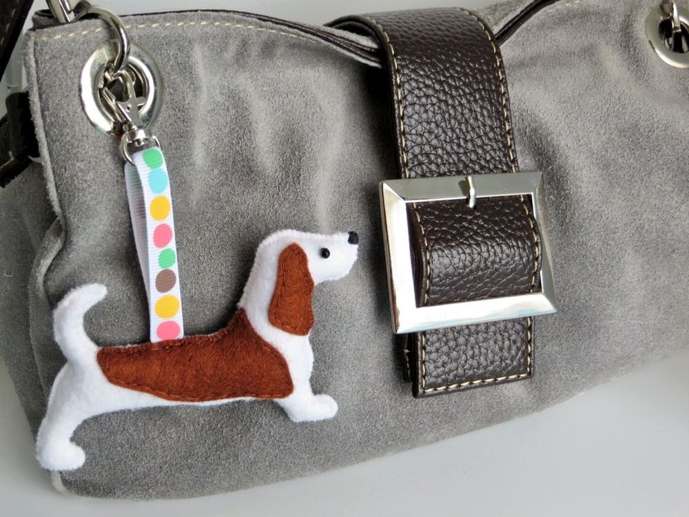 A handmade felt basset hound dog charm by misheleneous attached to a grey suede handbag
