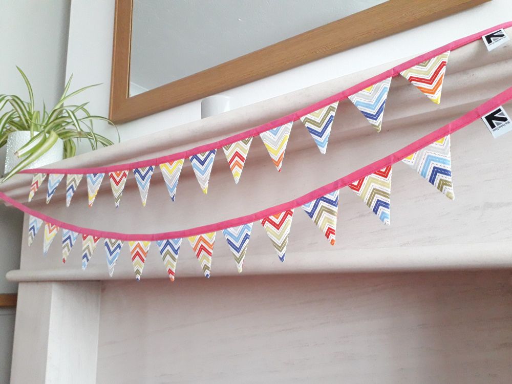 A pair of rainbow chevron fabric bunting garlands by misheleneous. Displayed on a fireplace mantlepiece