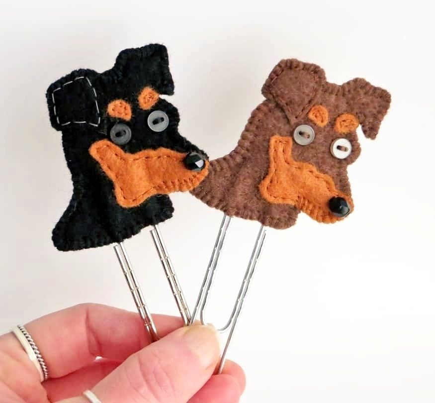 A pair of handmade felt miniature pinscher dog head planner clip bookmark by misheleneous held between finger and thumb