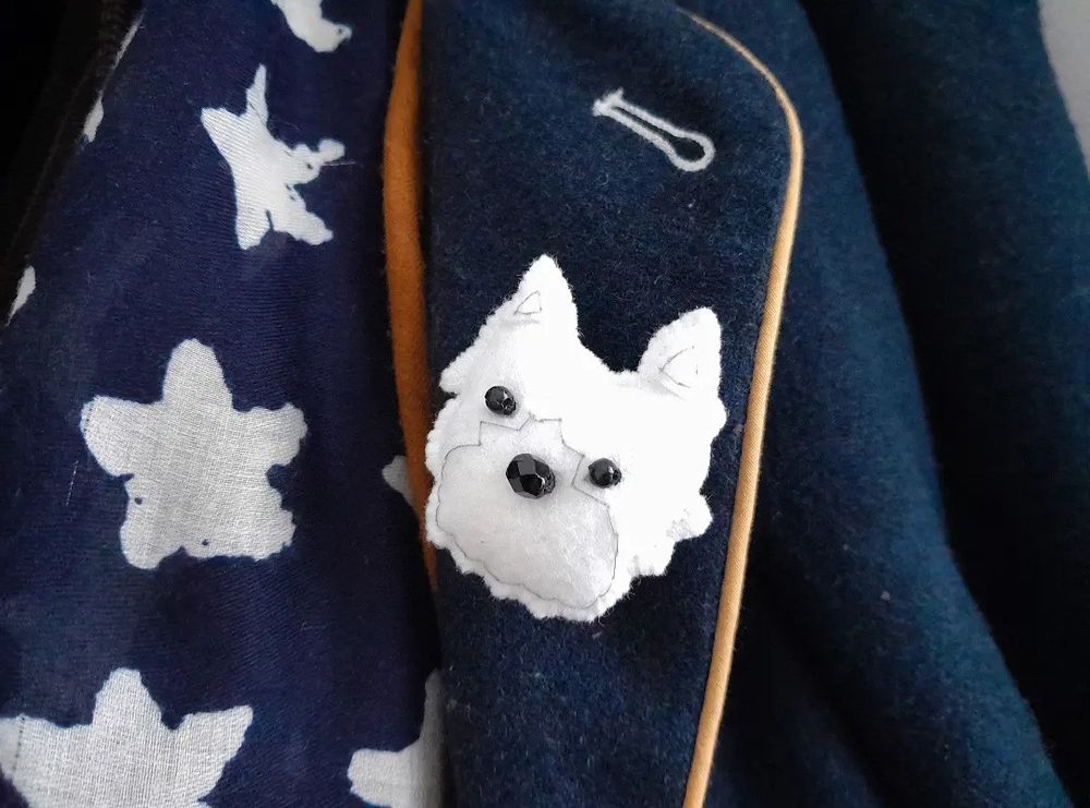A handmade felt westie dog head brooch pin by misheleneous attached to a navy wool jacket lapel
