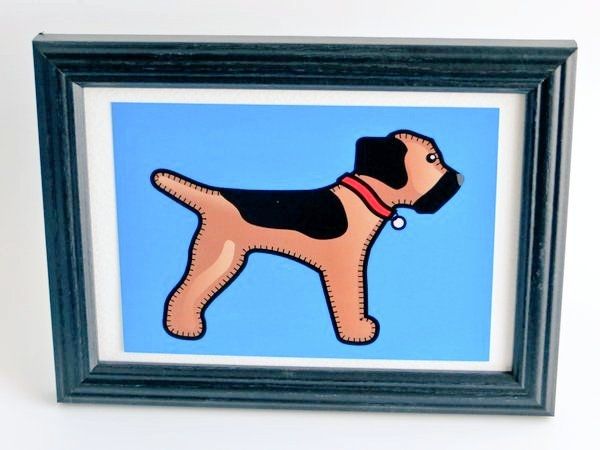 A blue A6 postcard print of the misheleneous border terrier logo dog in a black frame