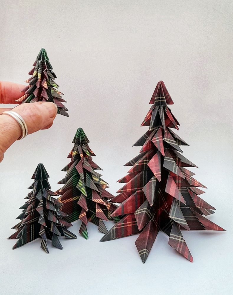 A collection of red and green tartan origami fir trees that I make at christmas with my the smallest and most difficult pictured between my thumb and fingers on the left
