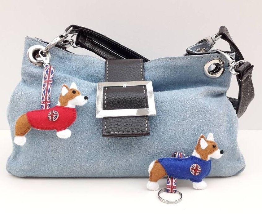 A pair of handmade felt pembroke welsh corgi dog charms by misheleneous. Wearing a red and blue jumper with a union jack flag motif and matching ribbon.  Attached to a pale blue suede handbag