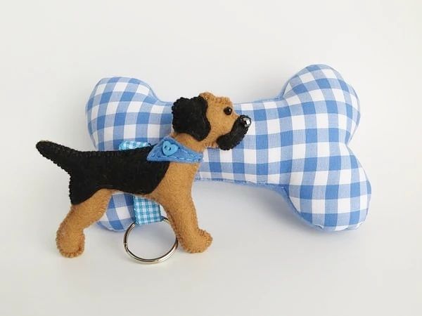 A handmade felt Blue and Tan border terrier keyring by misheleneous in front of a blue fabric gingham dog bone