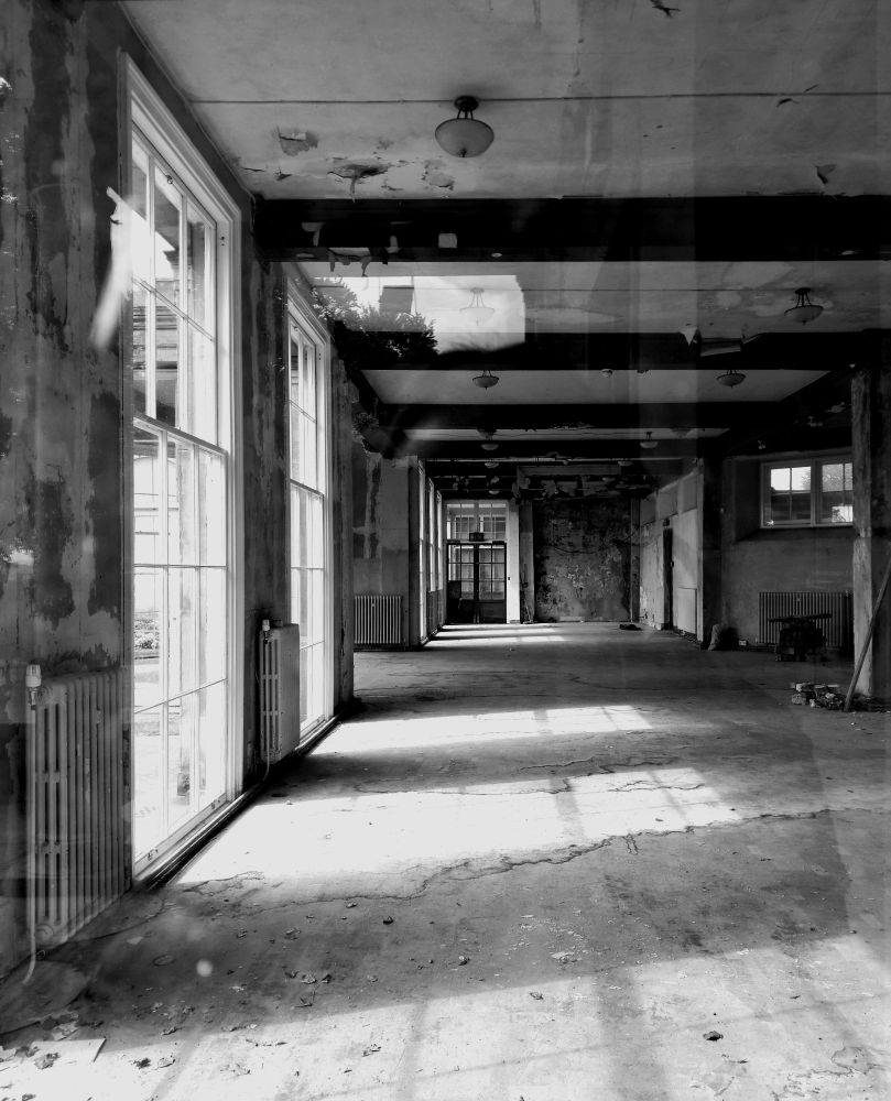 A black and white shot taken through a glass door of the inside of The Orangery at Heaton Hall, Heaton Park, Manchester. It shows an empty, quiet room badly in need of restoration 