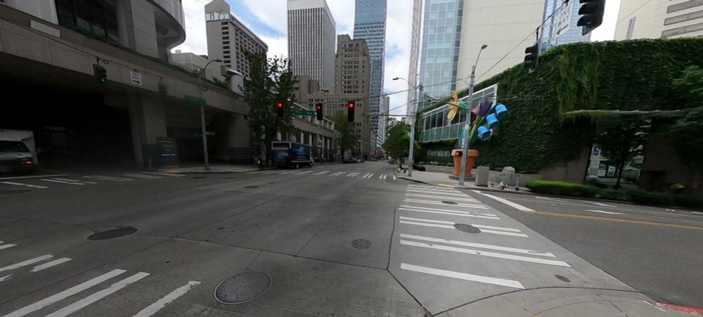 image 2/7 looking at intersection with flower pot to the right across street with parking garage on the left across street.