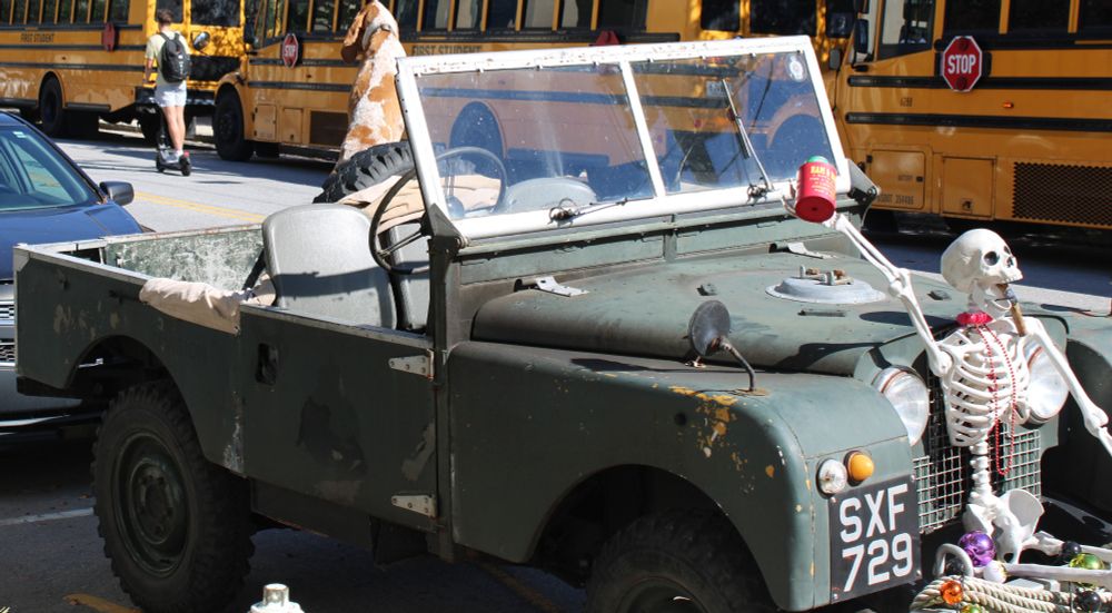 A dog in the back of a 1957 Land Rover looking at a scooter ride back