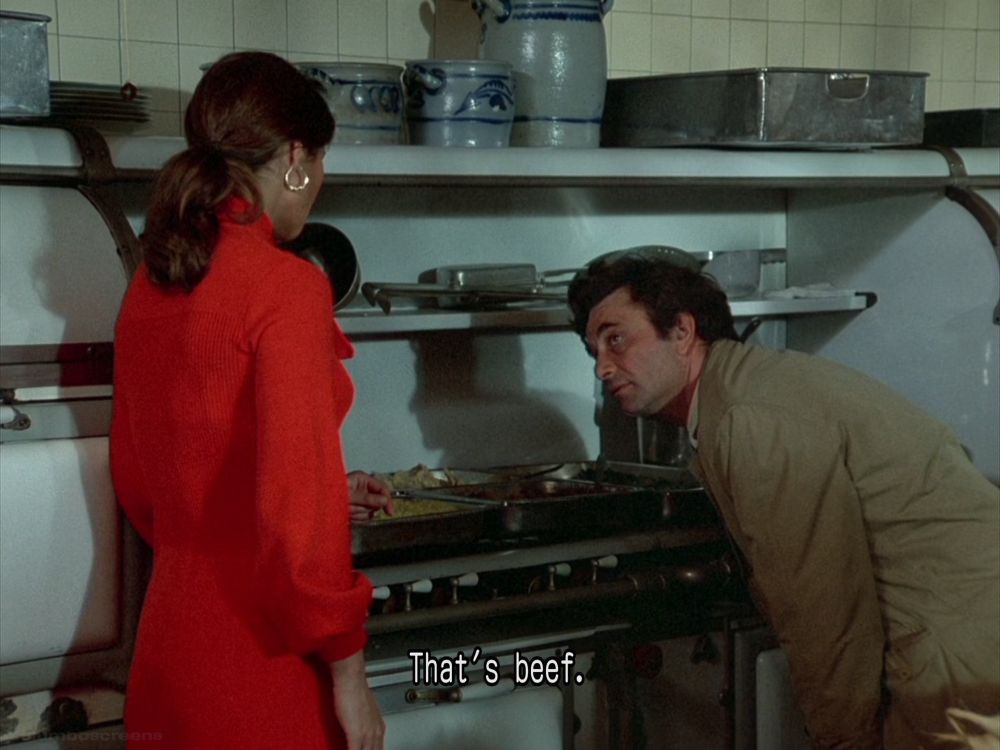 Same as before, Columbo in a kitchen with the woman in a red outfit. He’s leaning over the gas hob. Closed caption reads: “That’s beef.”