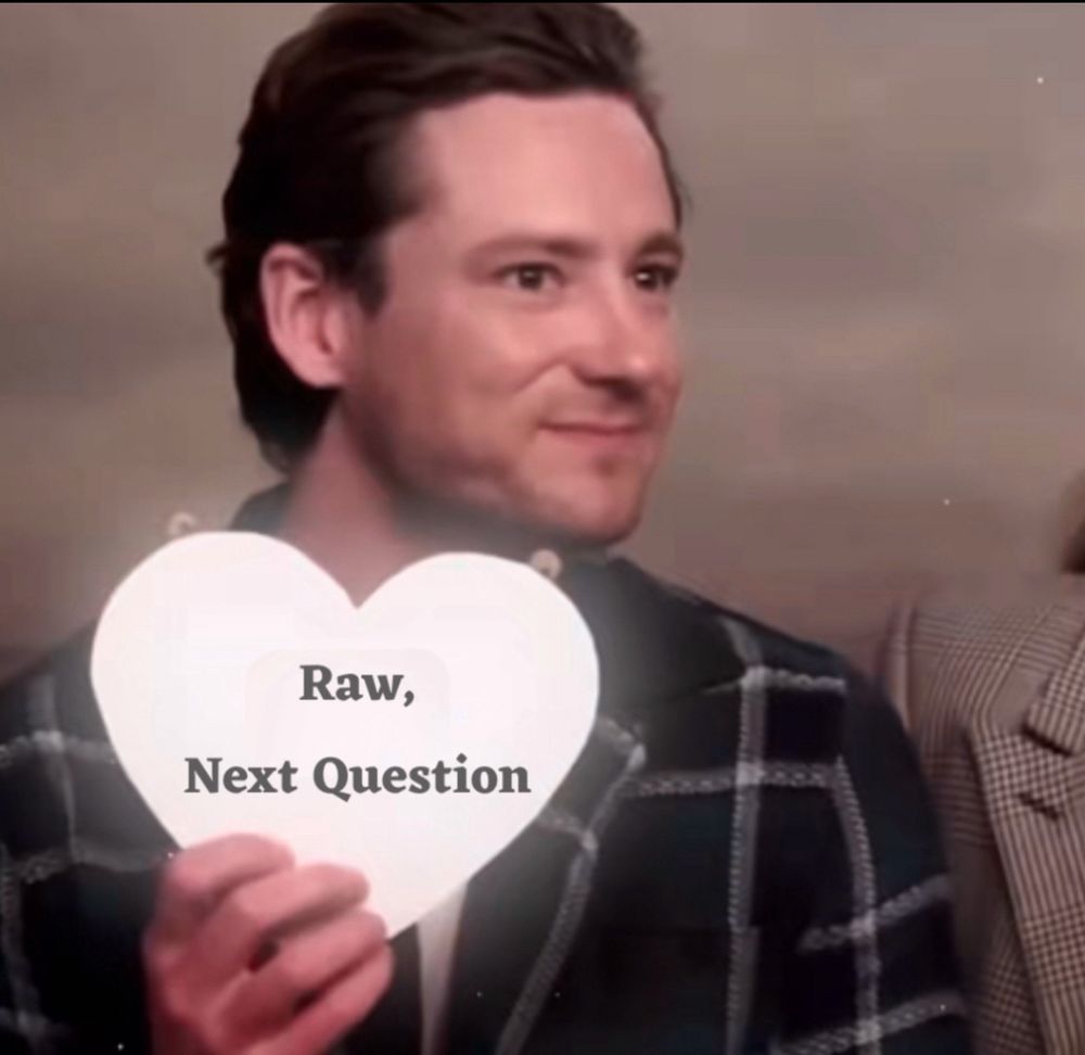 Lewis Pullman with a heart shaped cardboard with text saying “raw, next question”