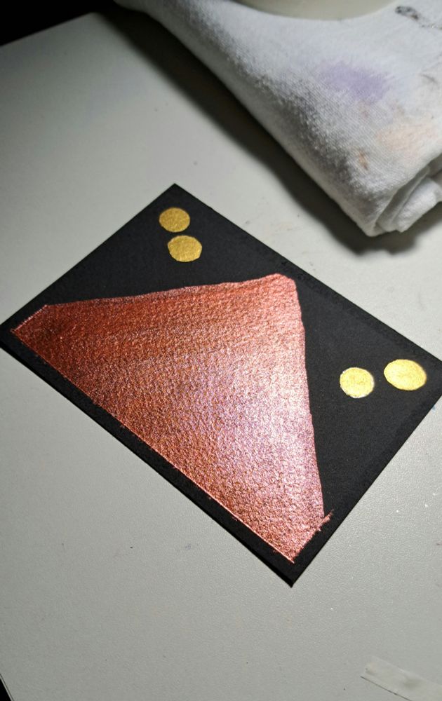A rectangle of black watercolor paper with a steep metallic Red Mountain and two round gold moons to either side